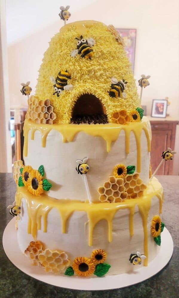 A whimsical three-tier honeybee cake topped with a sculpted hive and dripping with yellow glaze.