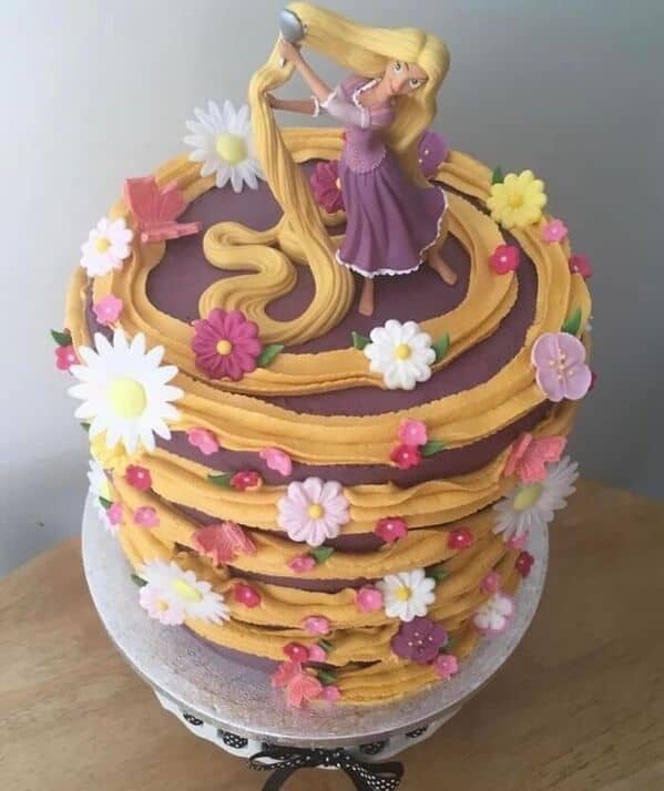 A Rapunzel themed cake with yellow frosting hair swirling around the sides decorated with flowers.