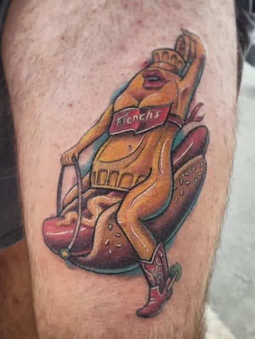 Detailed tattoo of a personified French’s mustard bottle wearing boots and riding a hot dog.