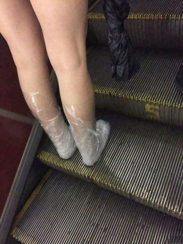 Person on an escalator with their bare feet and lower legs wrapped tightly in clear plastic wrap.