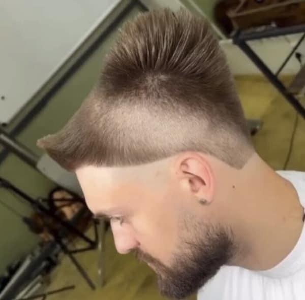 bad haircut showing a man with a buzzed fade on the sides and a massive, rigid block of hair sticking straight up and backward from his crown, resembling a solid ramp or aerodynamic spoiler.