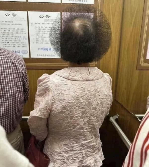bad haircut featuring a woman in an elevator with her dark hair heavily teased outwards into an impossibly perfect, massive, translucent sphere that looks like a static electricity experiment.