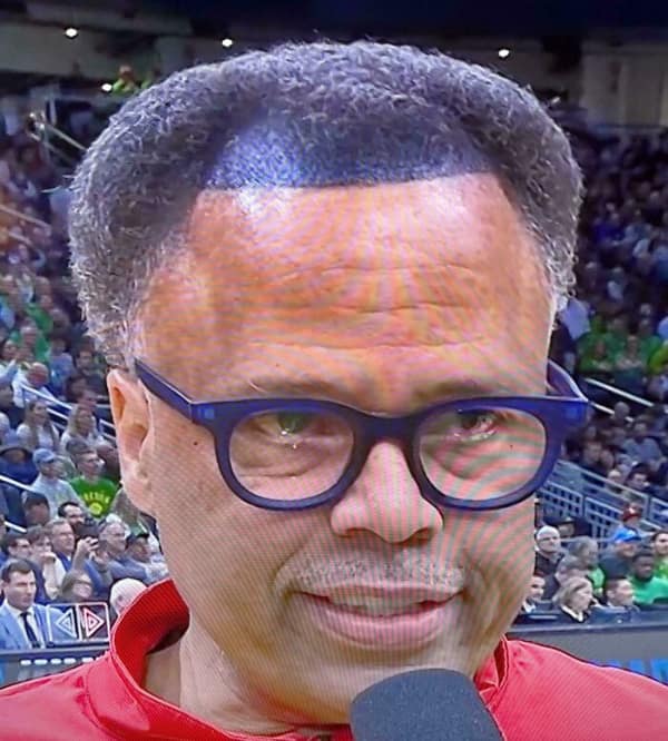 devastatingly bad haircut worn by a man on television, featuring a harsh, completely flat box cut that has receded halfway back on his scalp, revealing an unnatural, sharp blue dye line against his forehead.