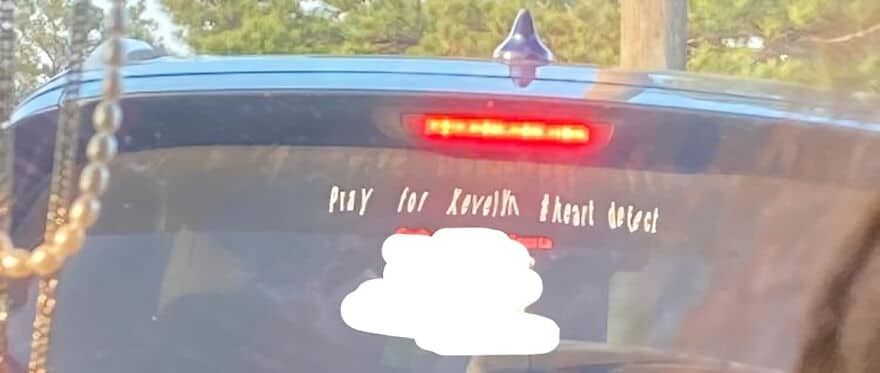 A car's rear window with a decal that reads Pray for Xevelyn heart defect.