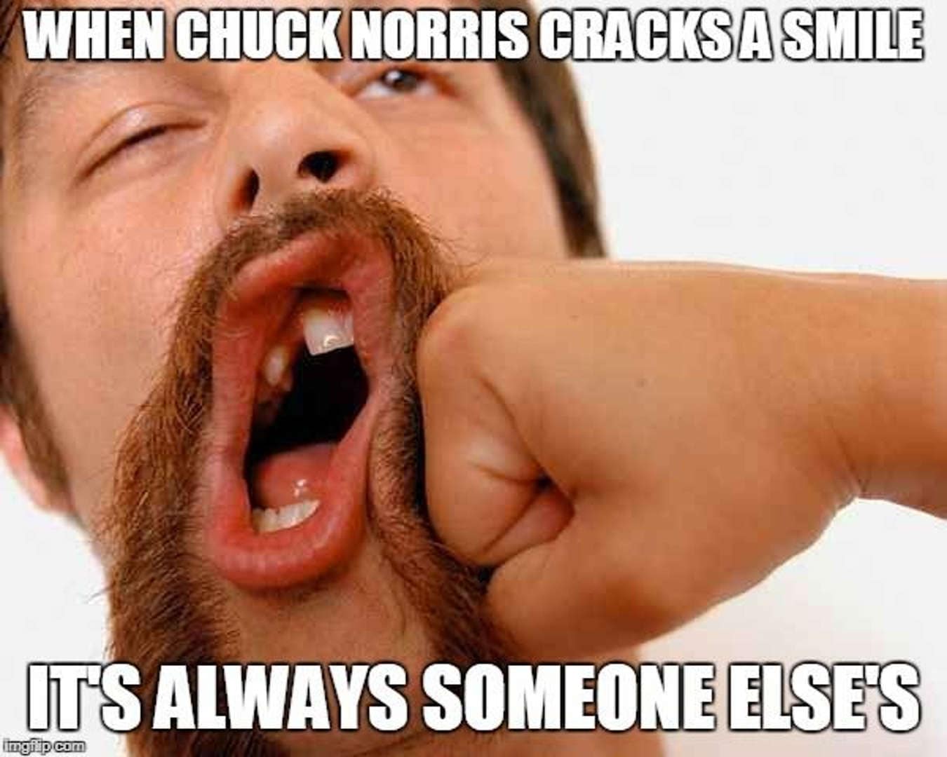 A visceral close-up of a fist smashing into a bearded man's mouth, sending teeth flying in a spray of spit. The caption on this best Chuck Norris meme candidate reads: "When Chuck Norris cracks a smile, it's always someone else's."