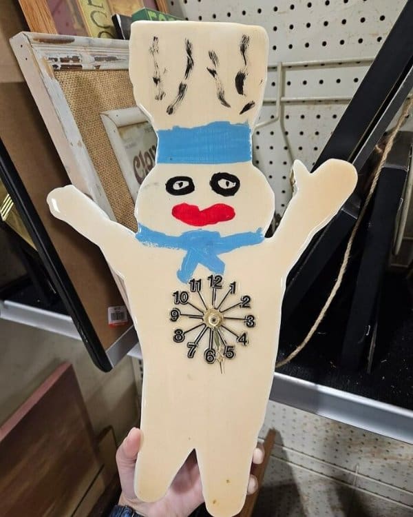 A DIY clock that is easily one of the best thrift store finds for nightmare fuel: a hand-painted wooden cut-out of the Pillsbury Doughboy featuring realistic human-like eyes and a smear of bright red lipstick.