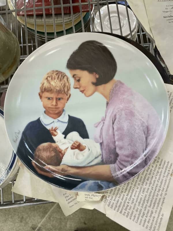 A decorative plate showing a woman holding a baby while a boy makes a funny face.