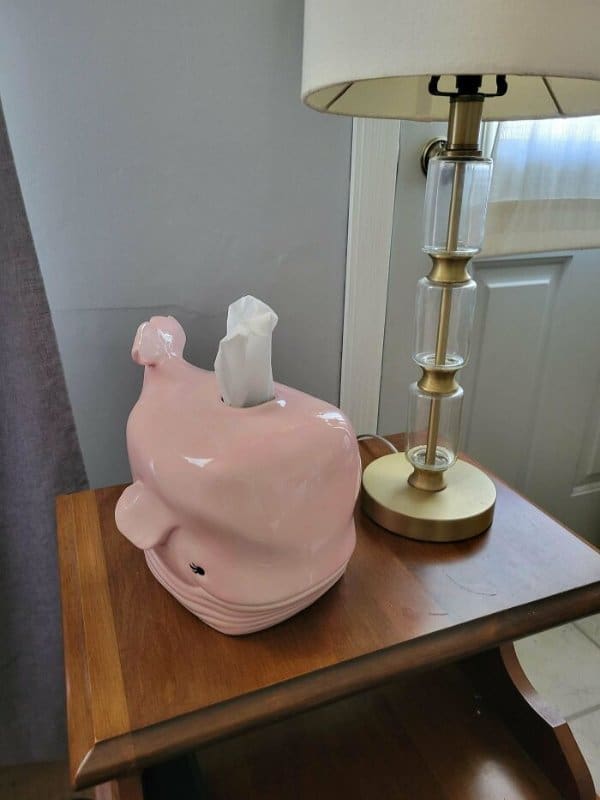 clever piece of home decor consisting of a glossy pink ceramic whale tissue box holder, positioned so that the tissues pull out through the blowhole on top of its head.