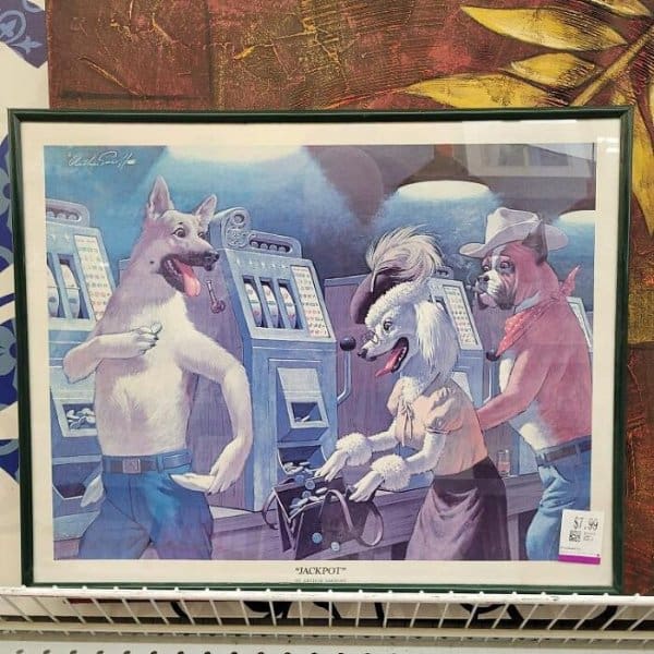 A framed kitschy print titled "JACKPOT," showing anthropomorphic dogs (a German Shepherd, Poodle, and Boxer) excitedly playing slot machines and collecting silver coins in a casino.