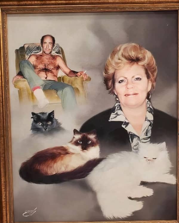 A framed portrait featuring a shirtless man in a recliner, a woman, and three cats.