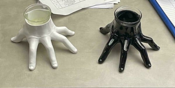 Two ceramic candle holders shaped like severed human hands—one matte white and one glossy black—resting on a desk like "Thing" from The Addams Family