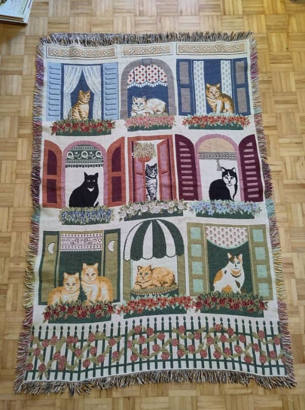 A woven tapestry rug depicting various colorful cats looking out of several different window frames.