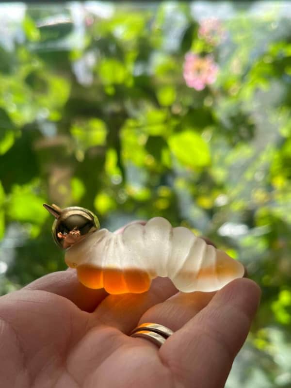 A hand holding a small frosted glass caterpillar figurine with a shiny gold head.