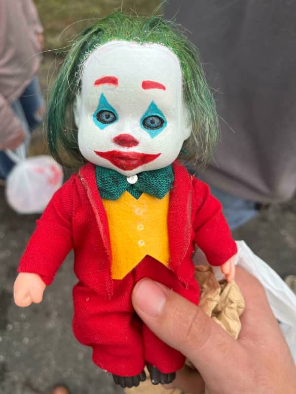 A hand holding a small doll repainted to look like the Joker with green hair.
