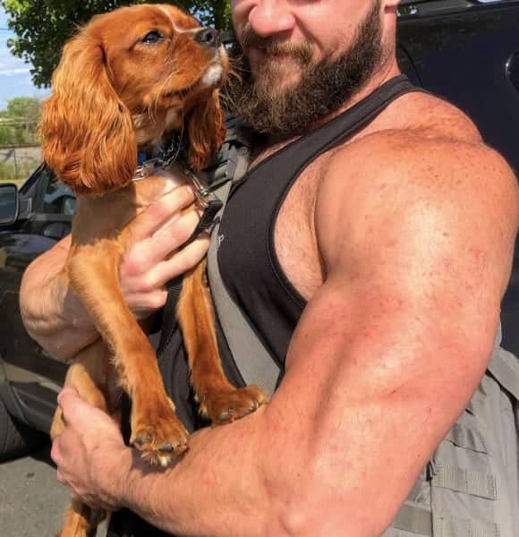 Bearded bodybuilder with massive arms holding small Cavalier King Charles Spaniel