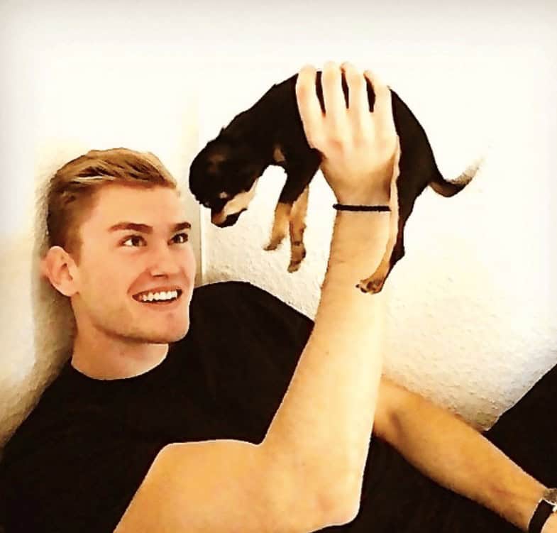 Smiling athletic blonde man holding up tiny black and tan Chihuahua puppy