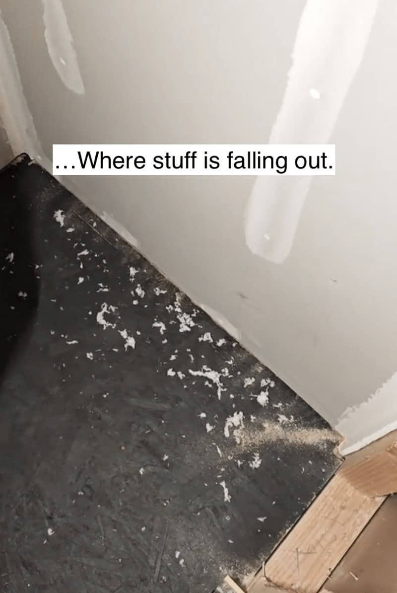 Debris and white insulation material falling out from behind unfinished drywall in a new construction.