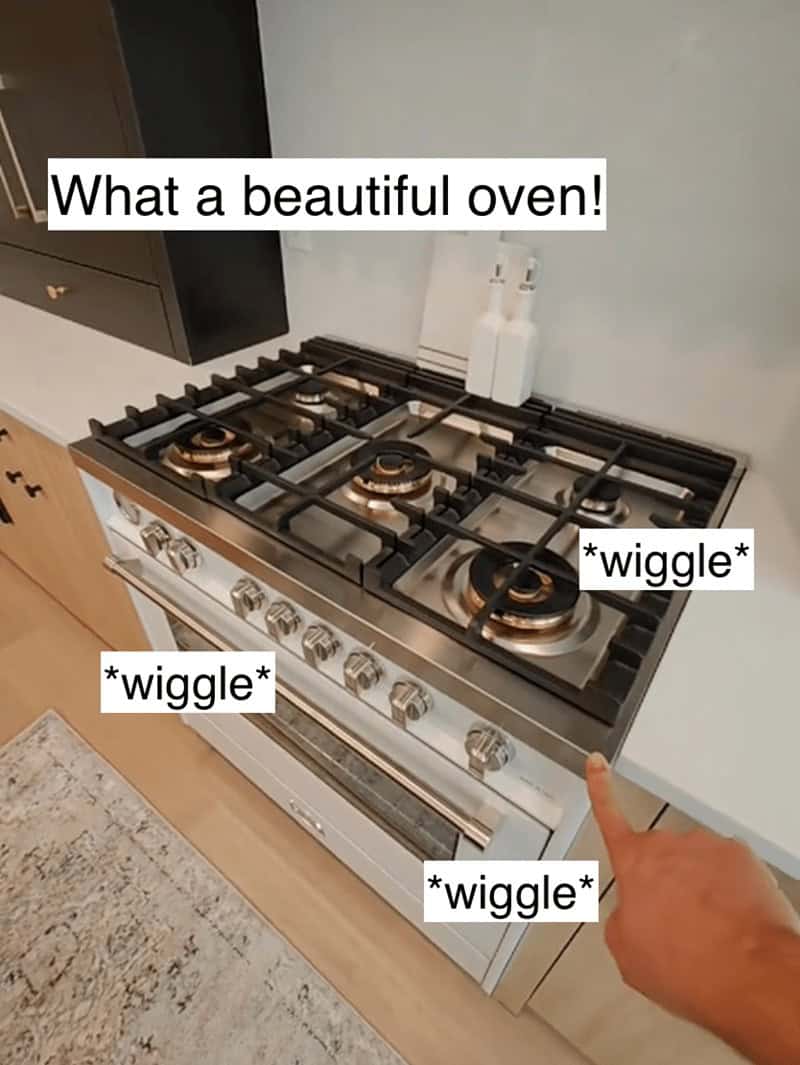Hand pointing at a wiggling gas stove range in a high-end kitchen with white cabinets.