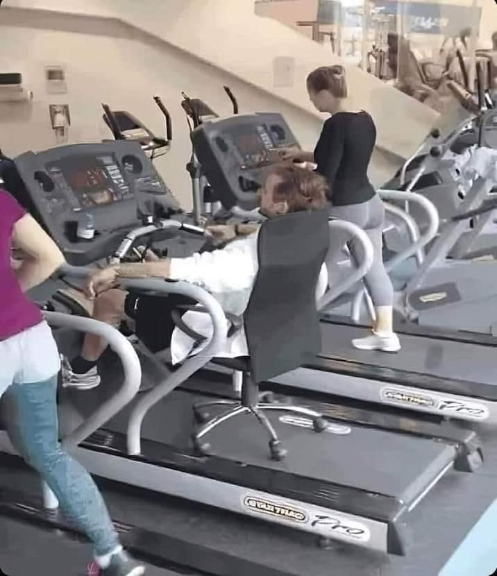 An unhinged and lazy gym hack defines this old meme where a man is seen relaxing in a rolling office chair while it's placed directly on top of a moving treadmill