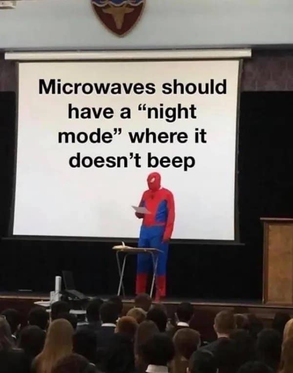 The old memes Spider-Man presentation format. A person in a full Spider-Man costume stands at a podium in a school hall. The projector screen behind them displays a universal truth: "Microwaves should have a 'night mode' where it doesn't beep."