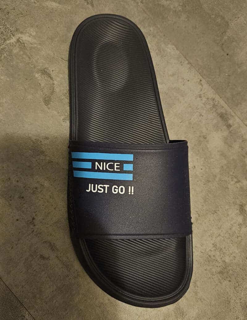 Black rubber slide sandal featuring a parody logo that says Nice and Just Go.