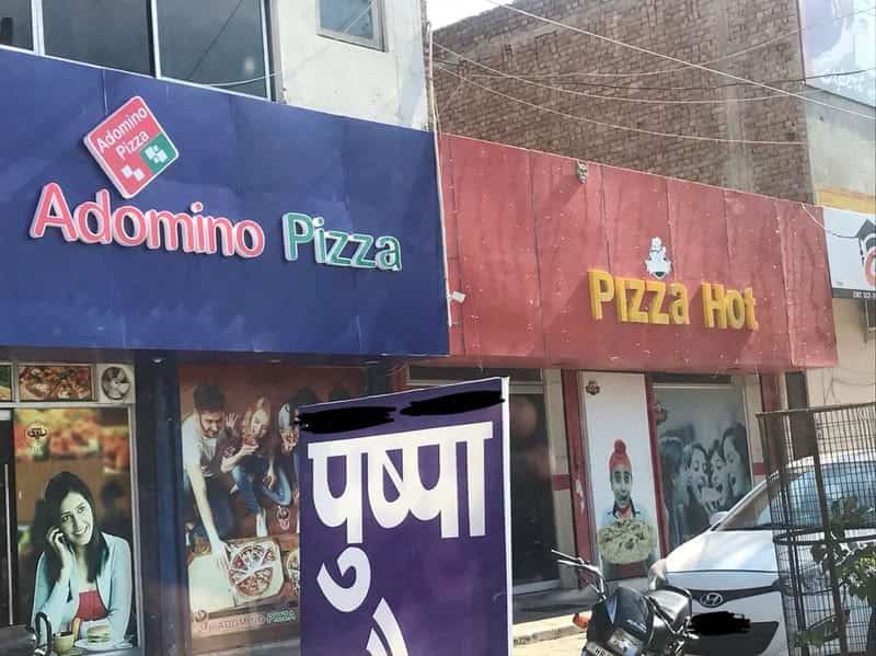Storefronts for pizza restaurants named Adomino Pizza and Pizza Hot located right next to each other.
