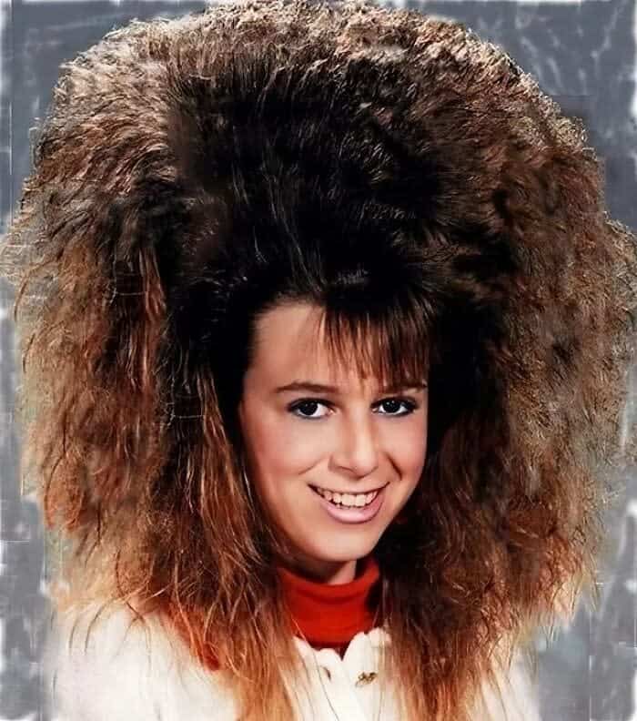 Teenager with massive, sky-high teased brown hair and bangs in a 1980s studio portrait.