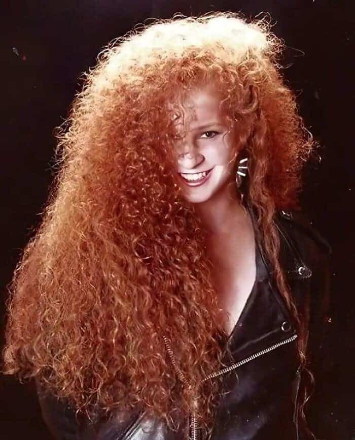 Smiling woman with very long, thick red curly hair and voluminous teased bangs.
