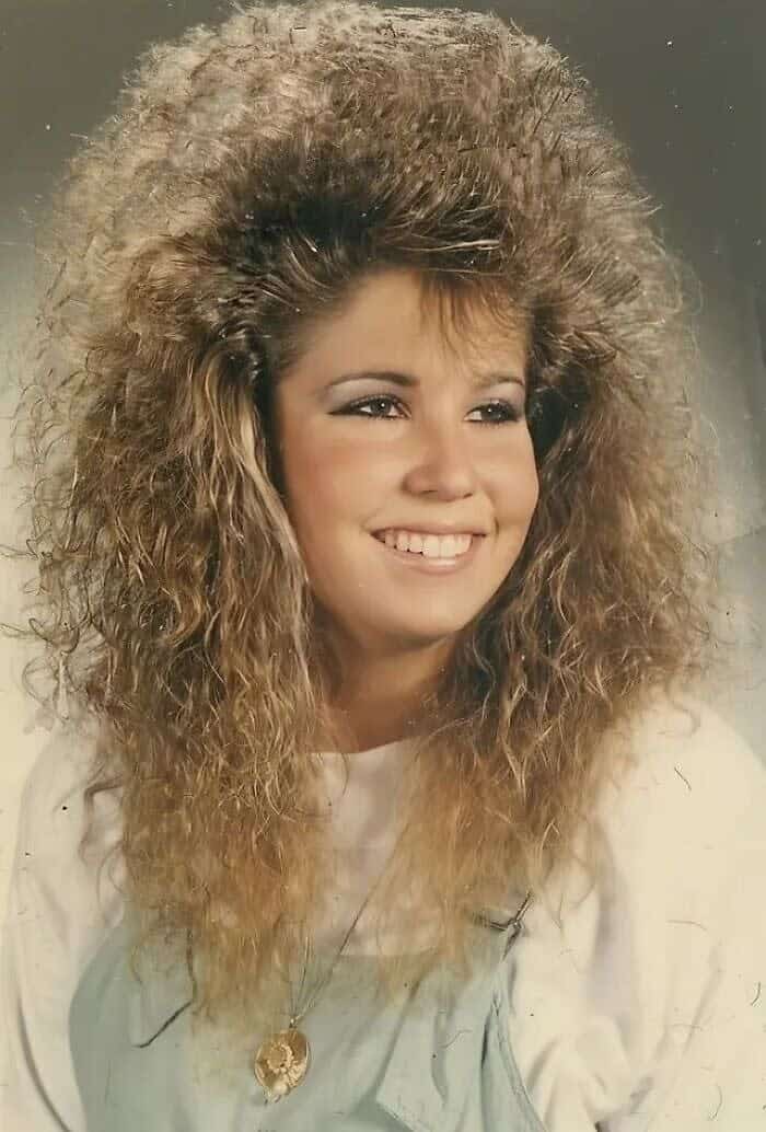 High school portrait of a girl with feathered, teased light brown hair reaching extreme heights.