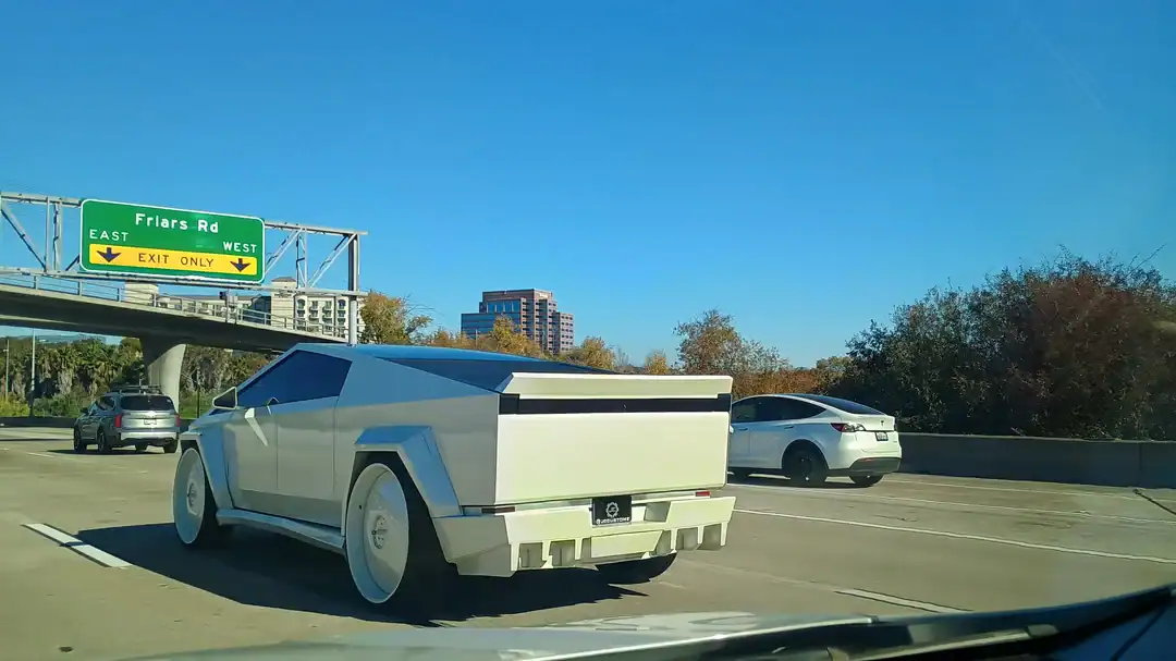 White Tesla Cybertruck modified with a widebody kit and massive white deep-dish rims on a highway.