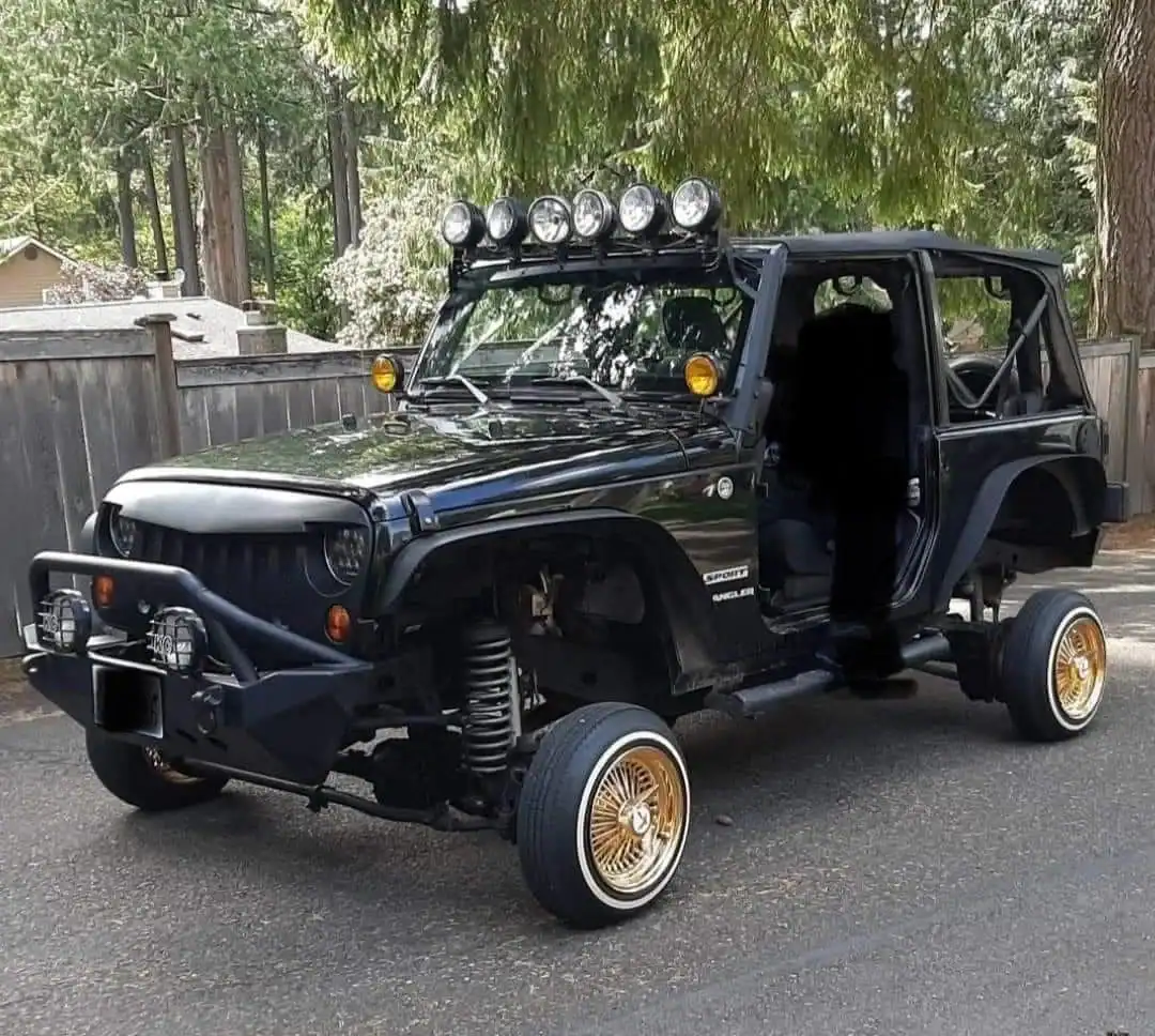 Black Jeep Wrangler modified with gold wire wheels, low-profile tires, and a significant suspension lift.