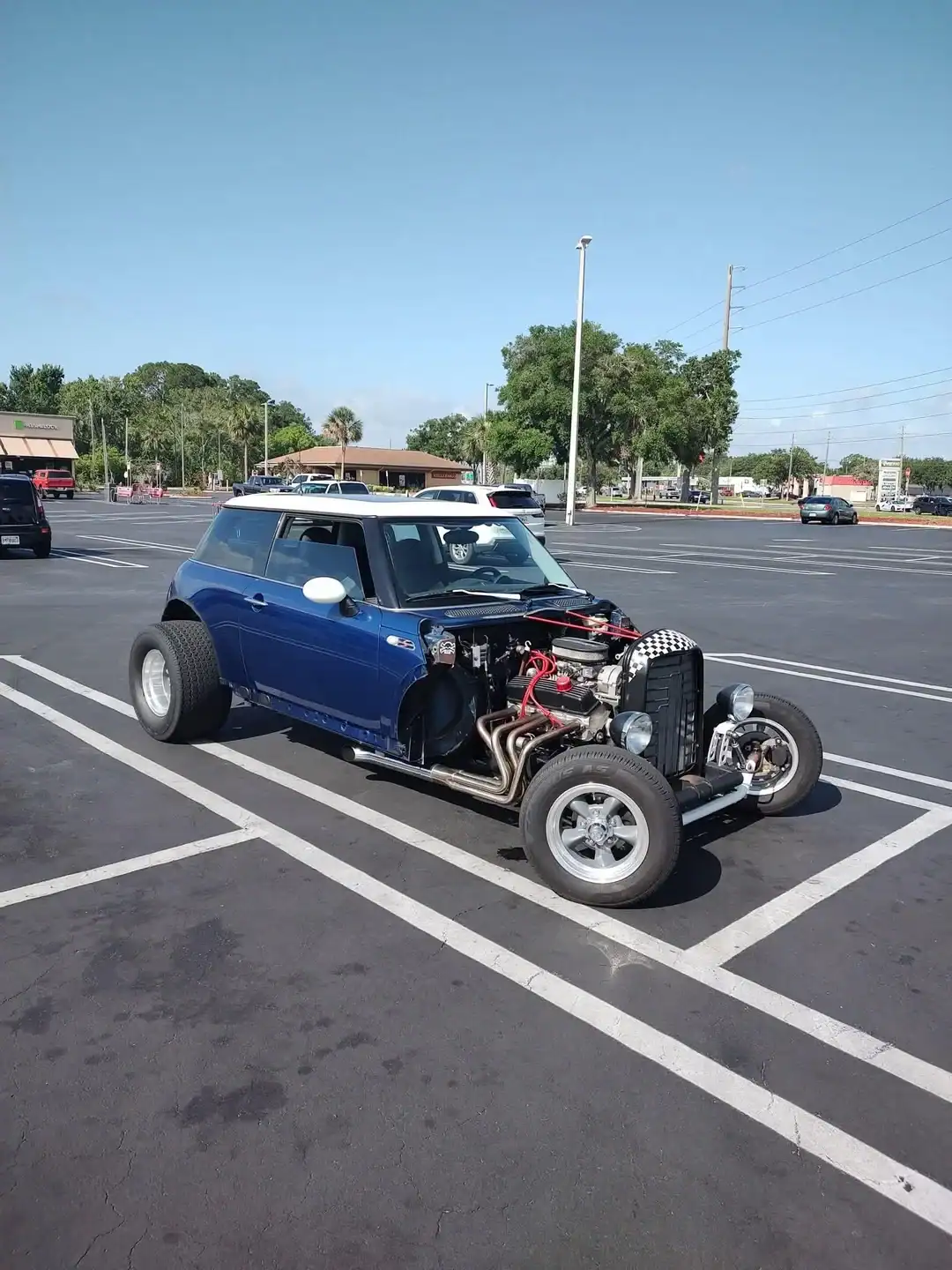 Blue Mini Cooper converted into a hot rod with an exposed engine and oversized rear tires.