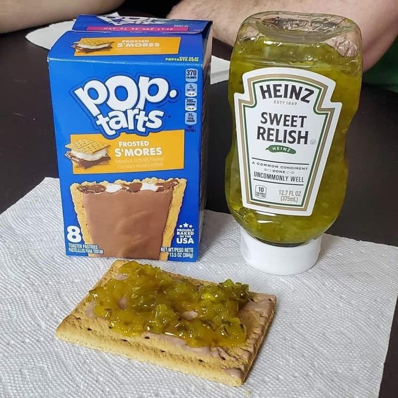 A real-life example of a cursed food creation shows a frosted S'mores Pop-Tart being used as a base for a thick, chunky layer of Heinz sweet pickle relish.