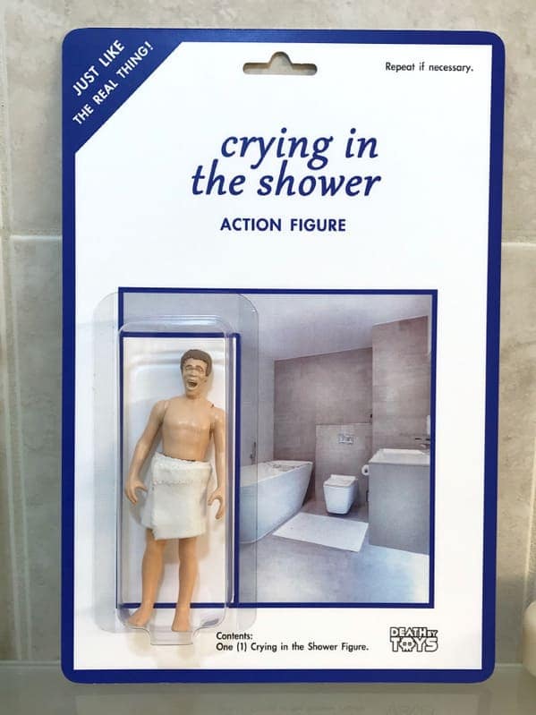 A satirical death by toys creation titled "crying in the shower ACTION FIGURE." The package features a miniature man wearing only a white towel with a distraught, weeping facial expression, accompanied by the cynical instruction to "Repeat if necessary."