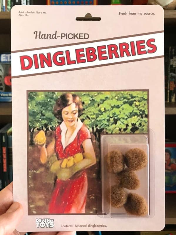 A gross-out funny fake action figure titled "Hand-Picked DINGLEBERRIES," marketed as being "Fresh from the source". The card art shows a vintage illustration of a woman picking fruit, while the product consists of several small, fuzzy brown balls.