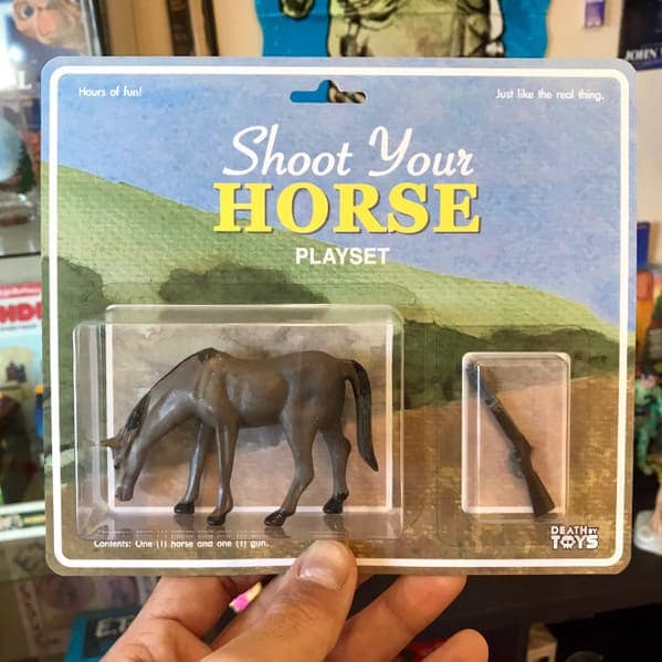 A bleak funny fake action figure playset titled "Shoot Your HORSE". The card art depicts a desolate green field, and the package contains a single plastic brown horse and a tiny, separate rifle.