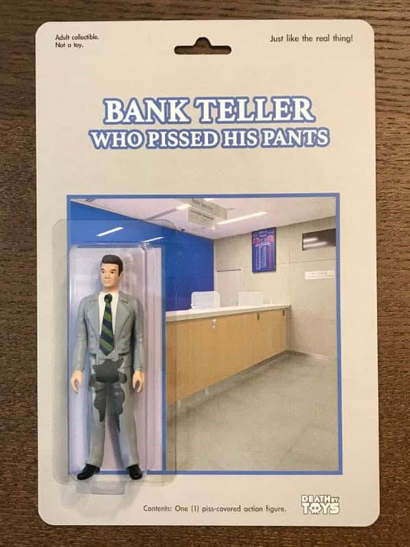 A humiliating death by toys figure titled "BANK TELLER WHO PISSED HIS PANTS". The small plastic man wears a grey suit with a large, prominent dark wet spot on the crotch, posed against a backdrop of a sterile bank interior.