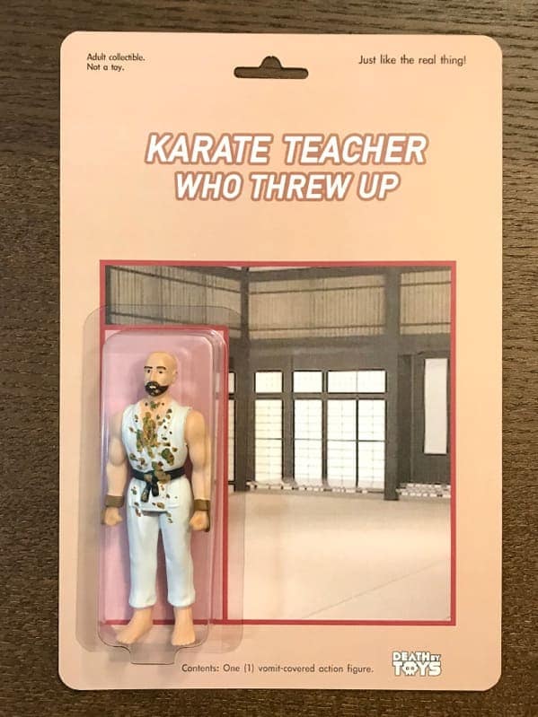 bizarre funny fake action figure labeled "KARATE TEACHER WHO THREW UP." The collectible features a bald, bearded man in a white martial arts gi covered in realistic green and brown vomit splatters, posed against a backdrop of a traditional dojo.