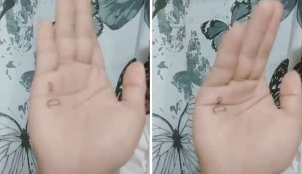 Faded and poorly executed tiny tattoo on a person's palm that is barely legible.