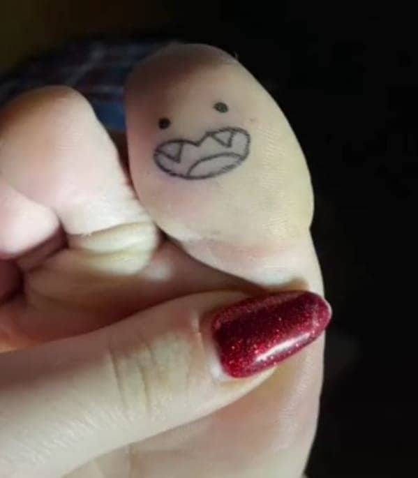 Close up of a big toe featuring a small monster face tattoo with fangs.
