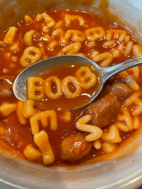 Spoon lifting alphabet soup letters out of a bowl of tomato broth and hot dogs to perfectly spell out immature anatomy jokes. Classic childish humor in this food meme.