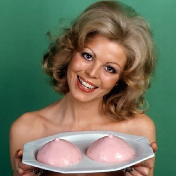 Retro 1970s woman smiling proudly while holding a plate of two pink gelatin desserts shaped suspiciously like human anatomy. Hilarious vintage savage food memes.