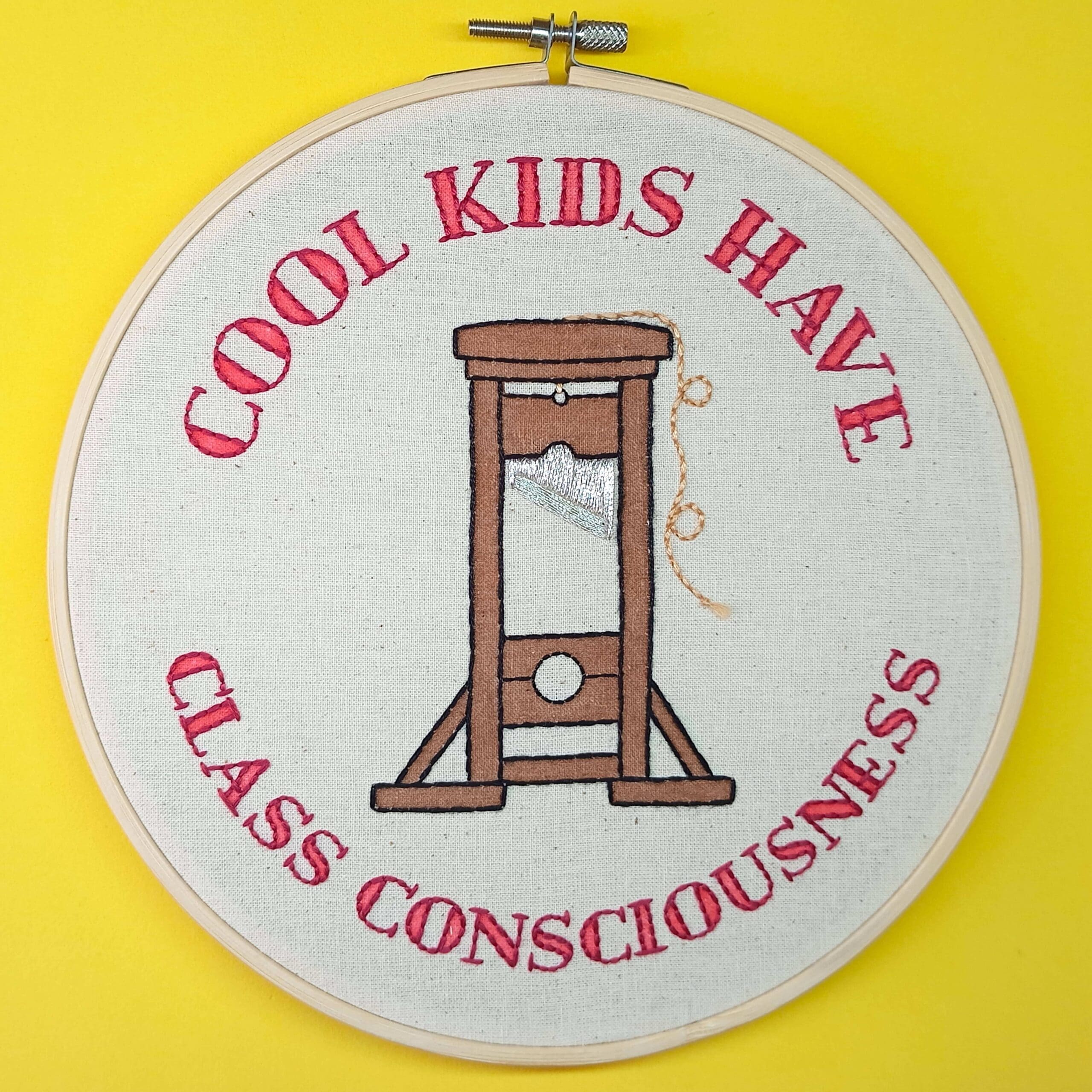 Needlework featuring a guillotine and the text "Cool Kids Have Class Consciousness" in red.