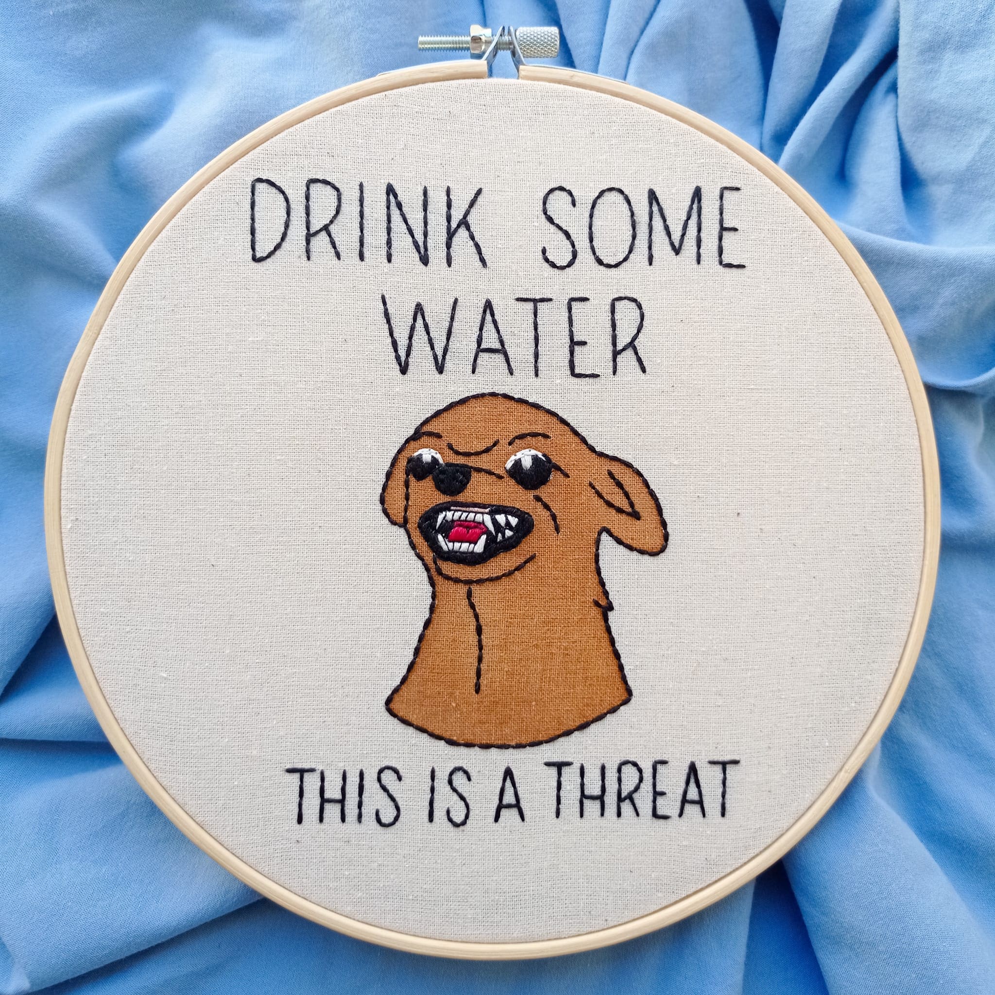 Embroidery of a snarling brown dog with the text "Drink Some Water: This Is A Threat."