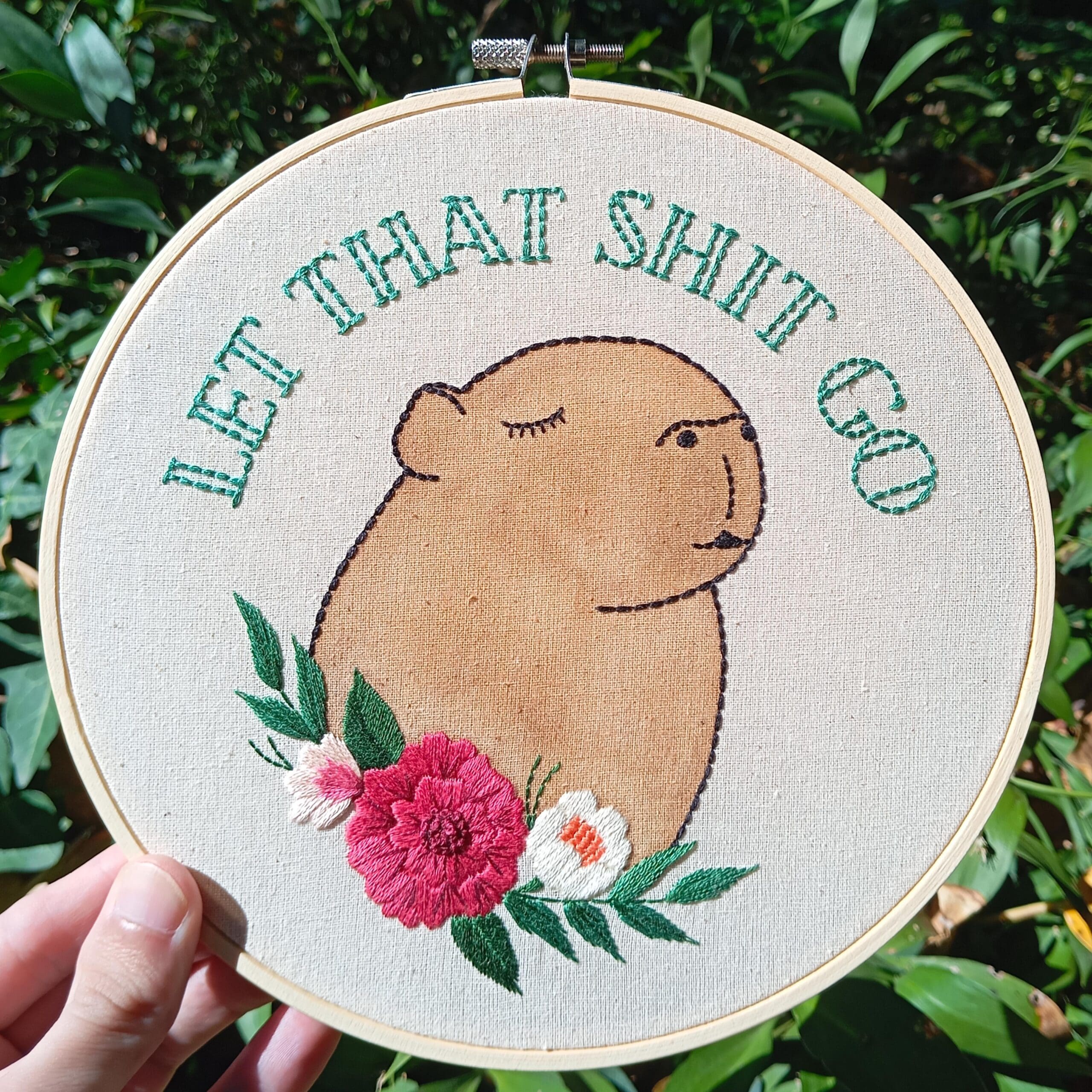 Needlework showing a calm capybara surrounded by flowers with the text "Let That Shit Go."