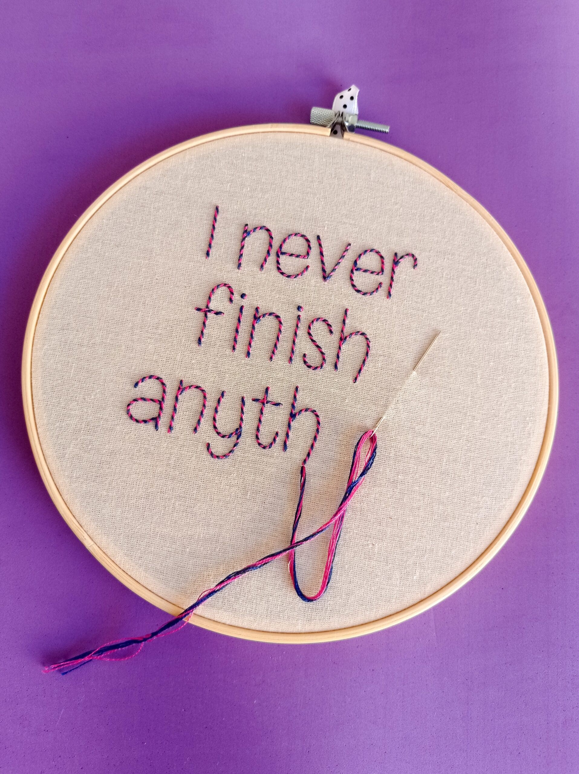 Needlework with the unfinished sentence "I never finish anyth" and an attached threaded needle.