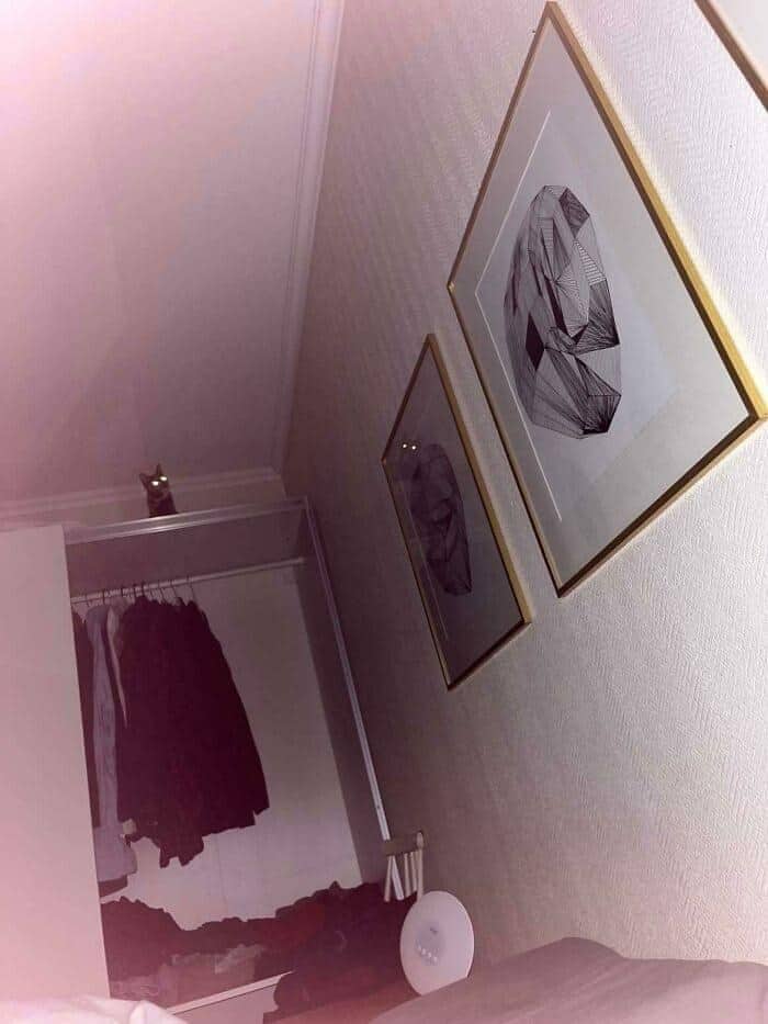 A slightly ominous entry in funny cat pictures showing a tiny feline hiding at the very top of a tall wardrobe, its eyes glowing brightly in the dark room.