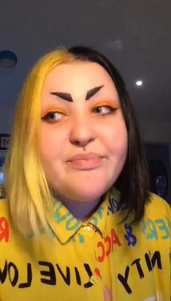 Woman with split dyed yellow and black hair sporting thick pointed geometric black eyebrows.