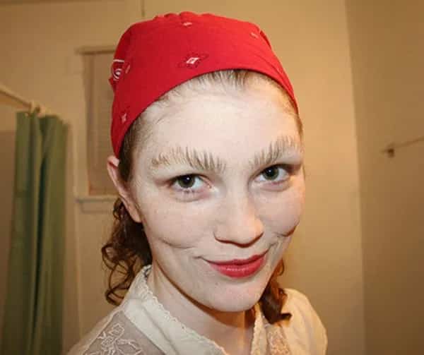 Woman wearing a red bandana with eyebrows styled into vertical spiky feathered points upward.