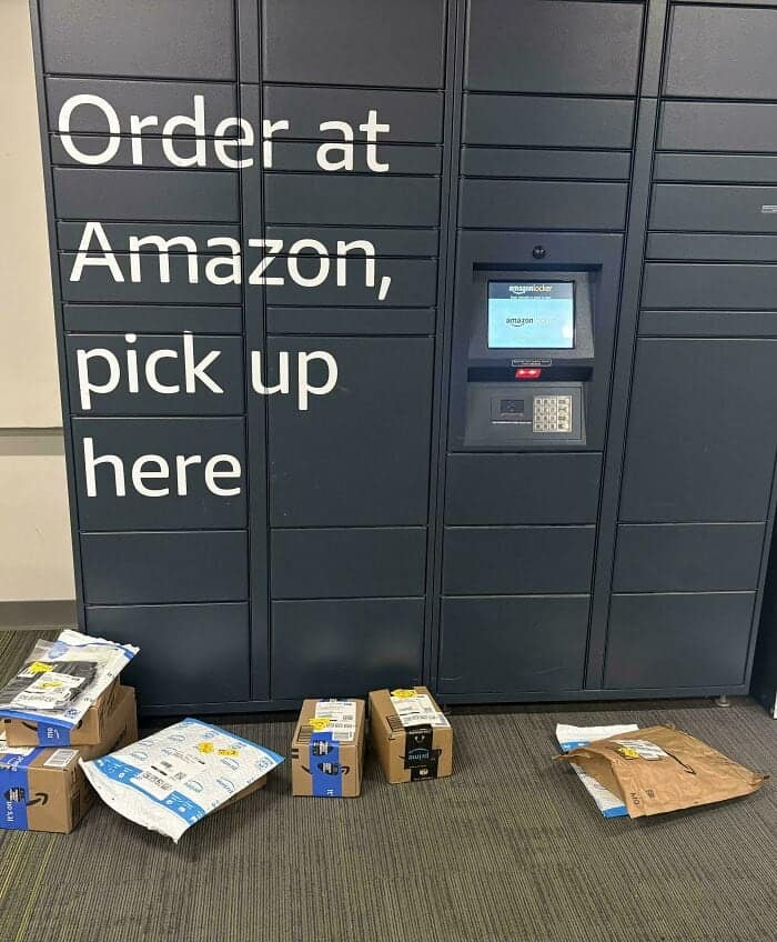 logistical funny fail at an Amazon locker station. Despite the large wall text that reads "Order at Amazon, pick up here," a pile of delivered packages has been left sitting on the floor directly in front of the locked compartments.